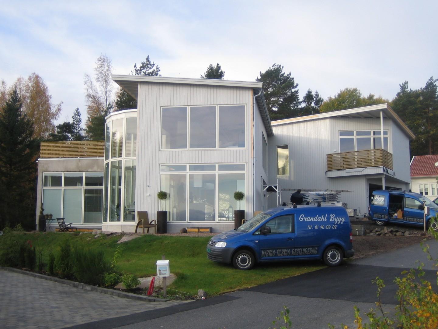 Hvitt hus med store vindusflater, med Grandahl Byggs varebil foran